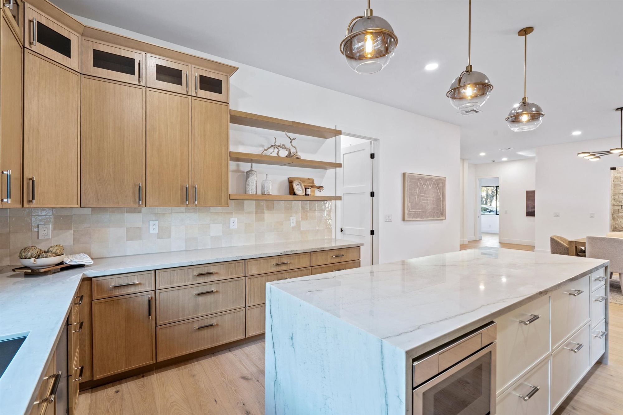 Kitchen with white oak cabinets, quartzite waterfall island and brass pendants